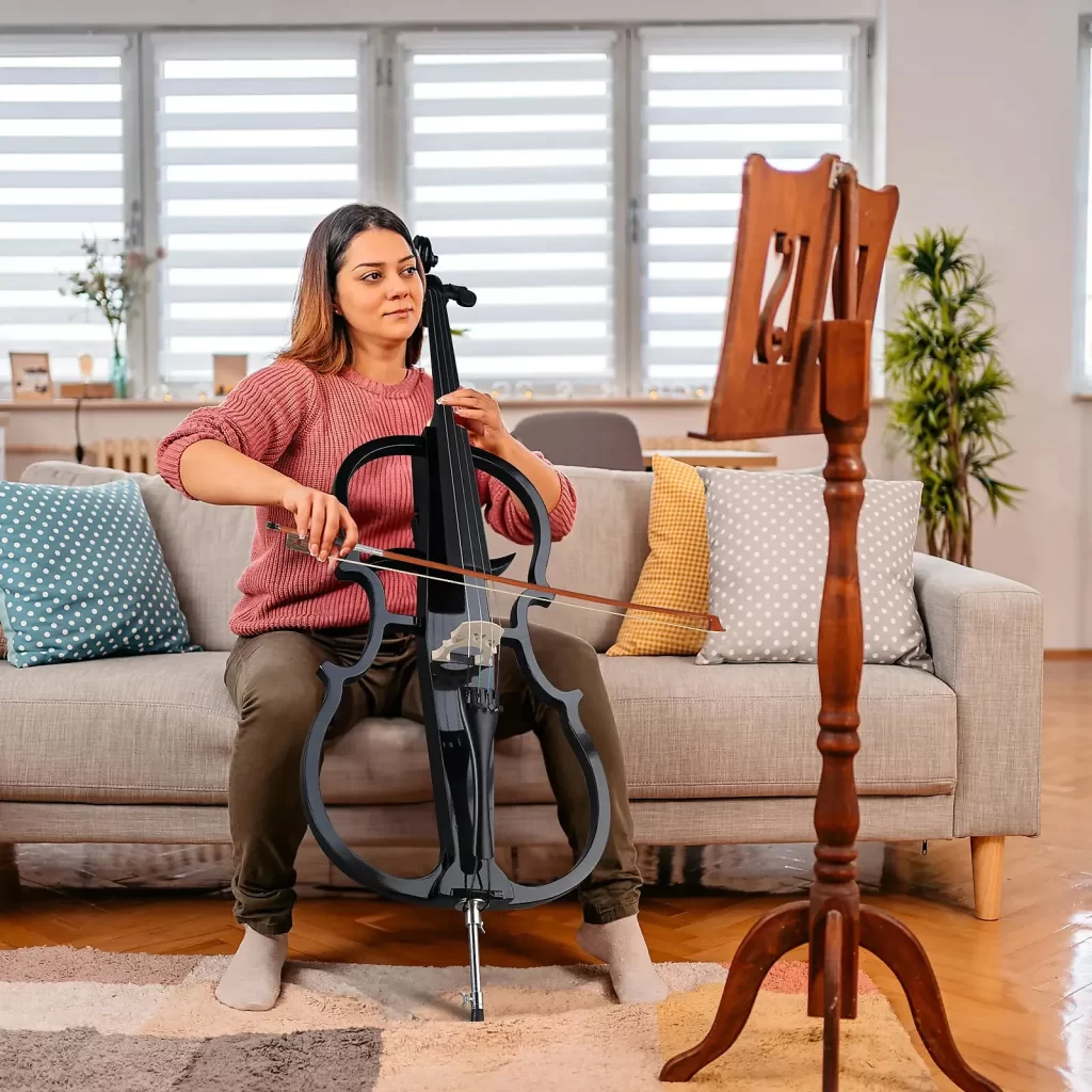 student beginner playing black electric cello music instrument at home on the couch practicing 